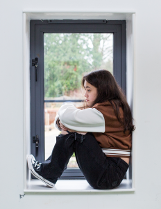 a girl sits on a windowsill, looking contemplative