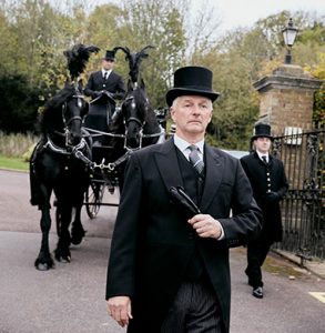 Funeral directors leading cortege of black horse drawn hearse